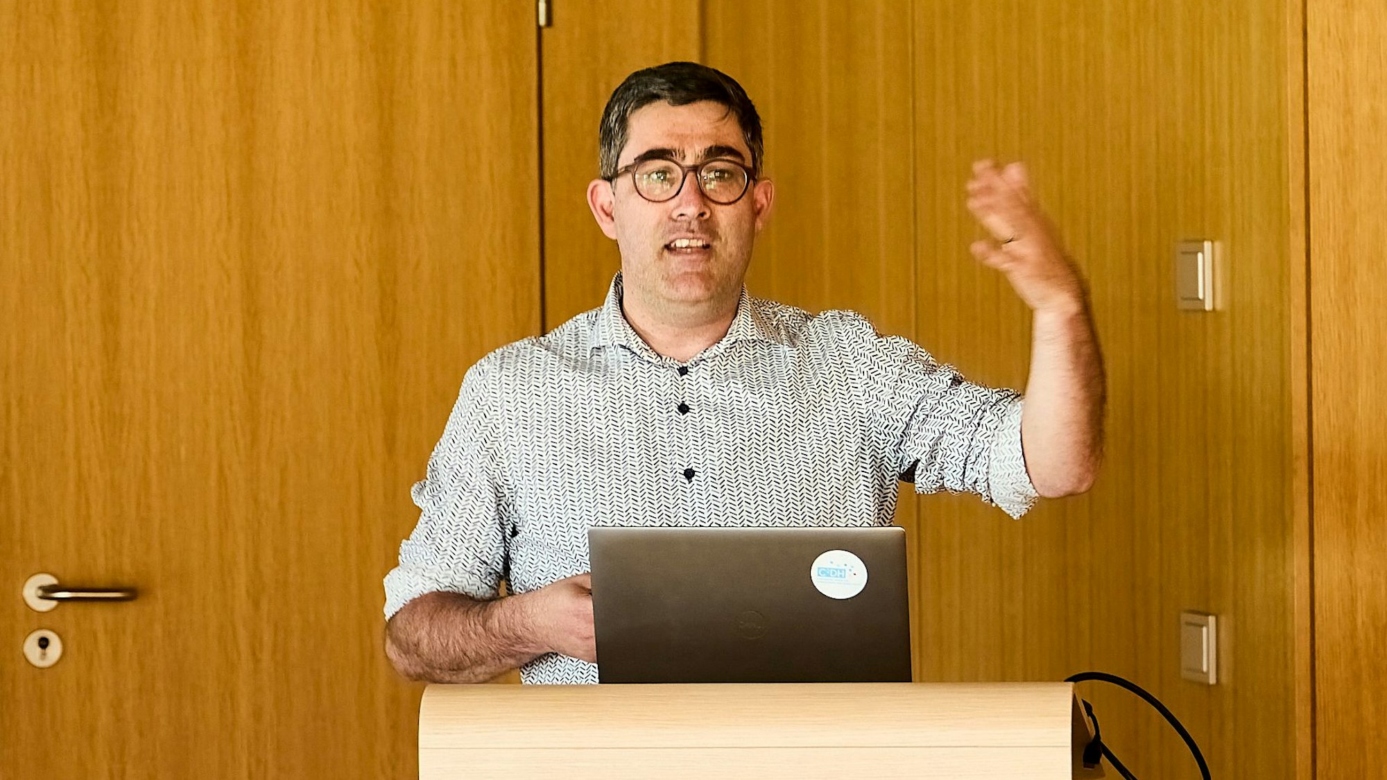 Professor Christoph Brüll steht in Vogelsang an einem Rednerpult und gestikuliert mit der linken Hand.