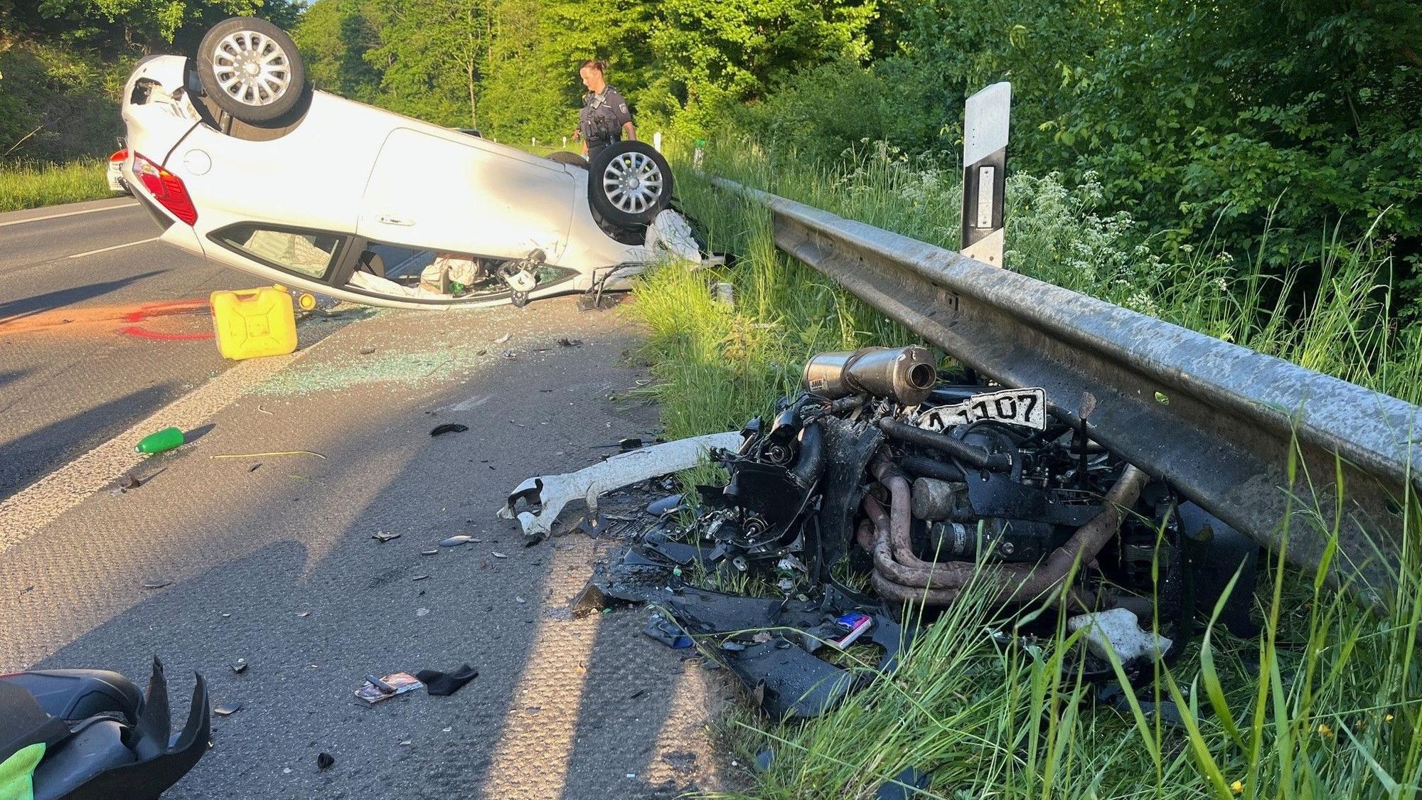 Ein zerstörtes Auto auf dem Dach und ein Motorrad an einer Unfallstelle