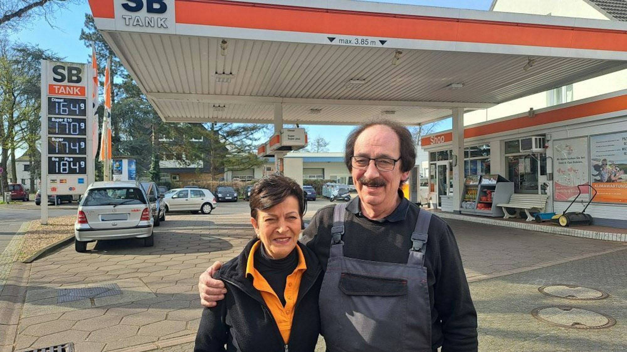 Eine Frau und ein Mann mit schwarzen Haaren stehen vor einer Tankstelle.