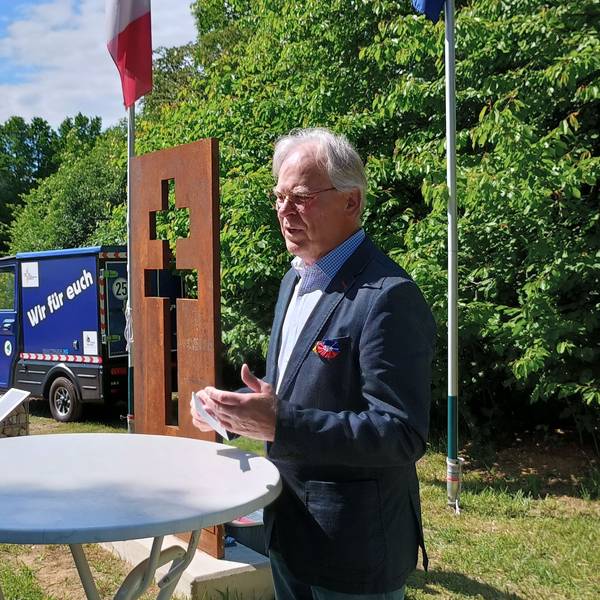Hübner steht schräg vor dem Lothringer Kreuz. Das Kreuz hat zwei Querbalken und ist als Lücke in einer rostigen Stahlplatte sichtbar.