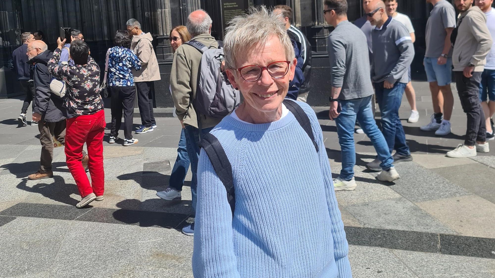 Jutta steht vor dem Kölner Dom und lächelt in die Kamera. Hinter ihr sind viele Menschen zu sehen.