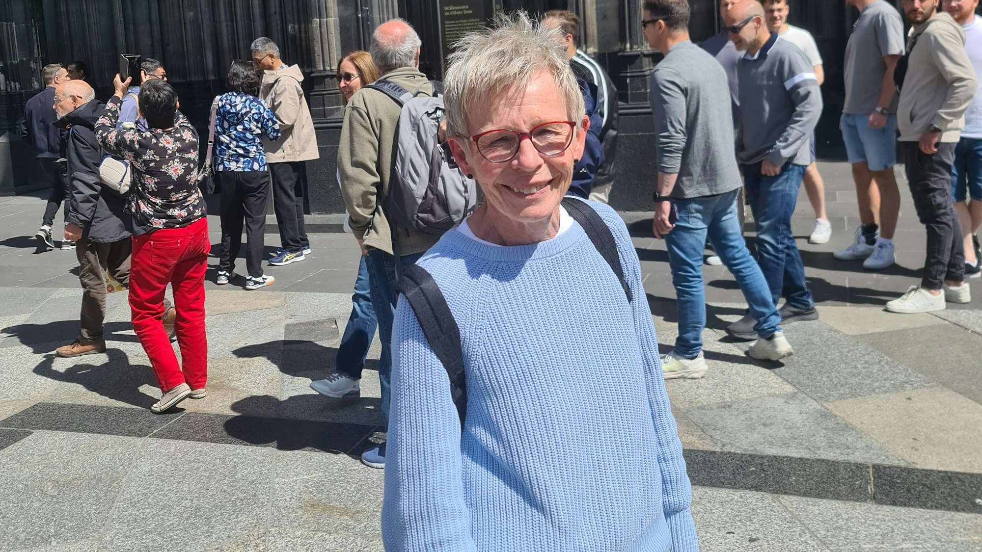 Jutta steht vor dem Kölner Dom und lächelt in die Kamera. Hinter ihr sind viele Menschen zu sehen.