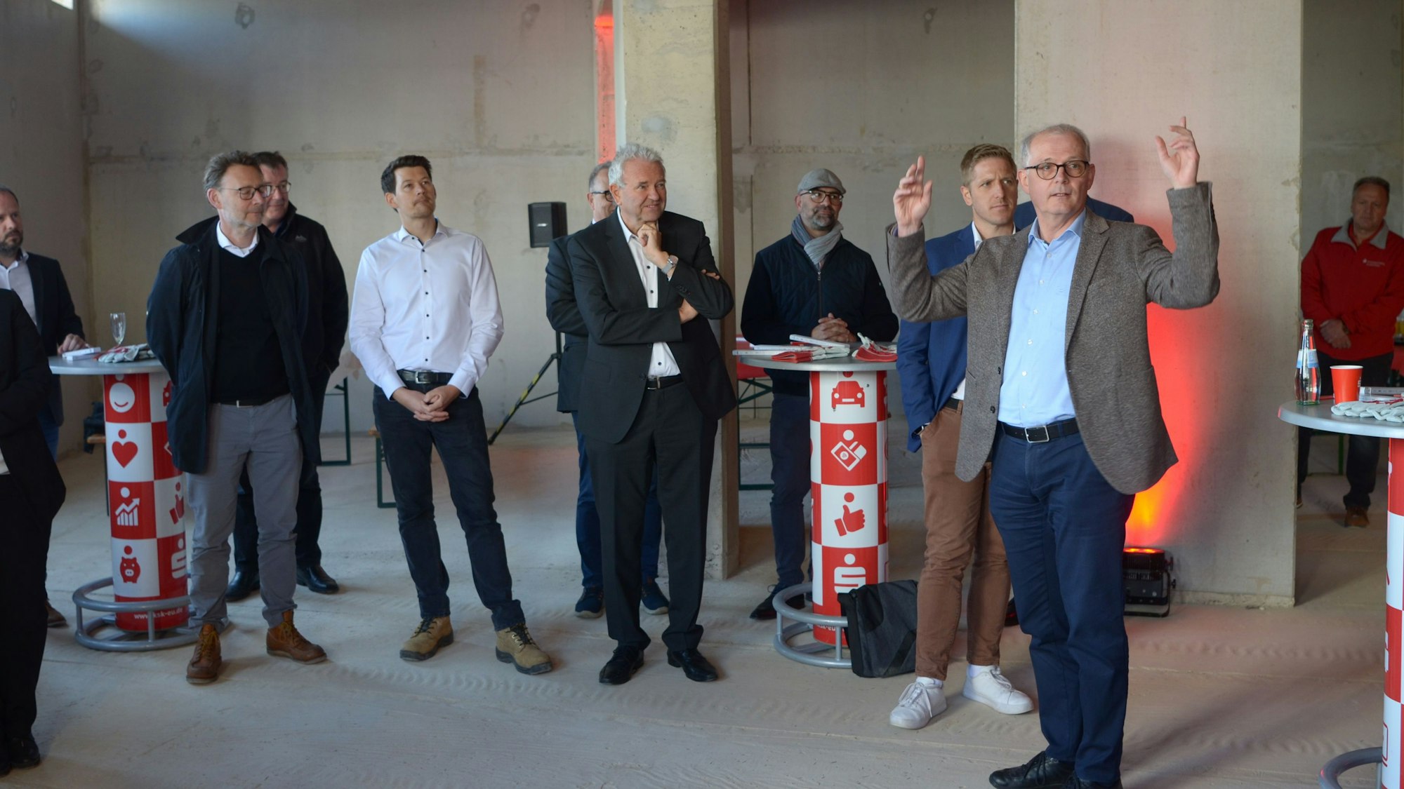 Mehrere Männer hören Holger Glück zu. Sie stehen in einem Rohbau.