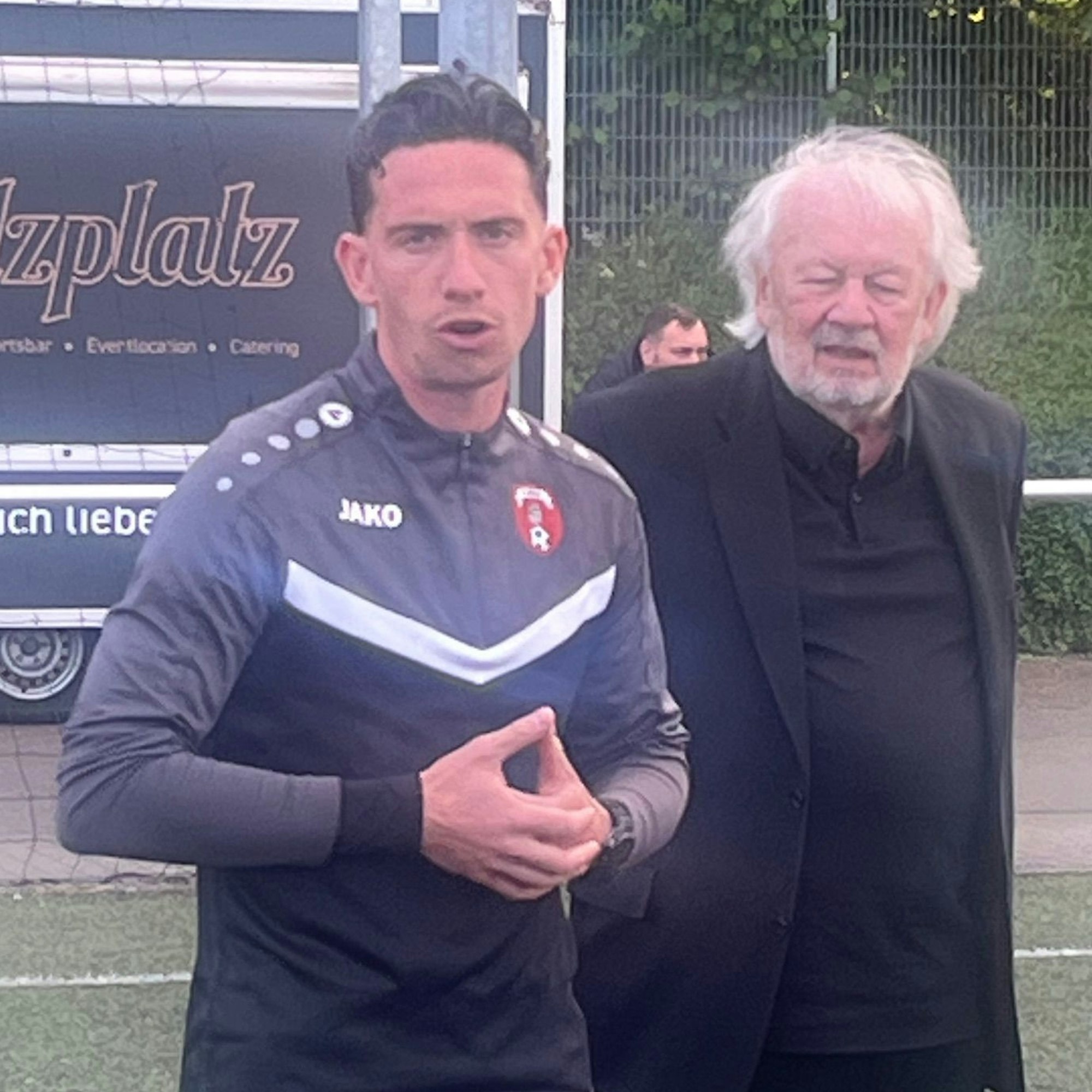 Ein älterer Mann stellt einen jungen Mann als neuen Trainer vor