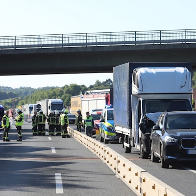 Ein Transporter und ein Pkw sind zusammengestoßen, dahinter staut sich der Verkehr, auf den gesperrten Spuren links daneben stehen Feuerwehrleute und Einsatzfahrzeuge.