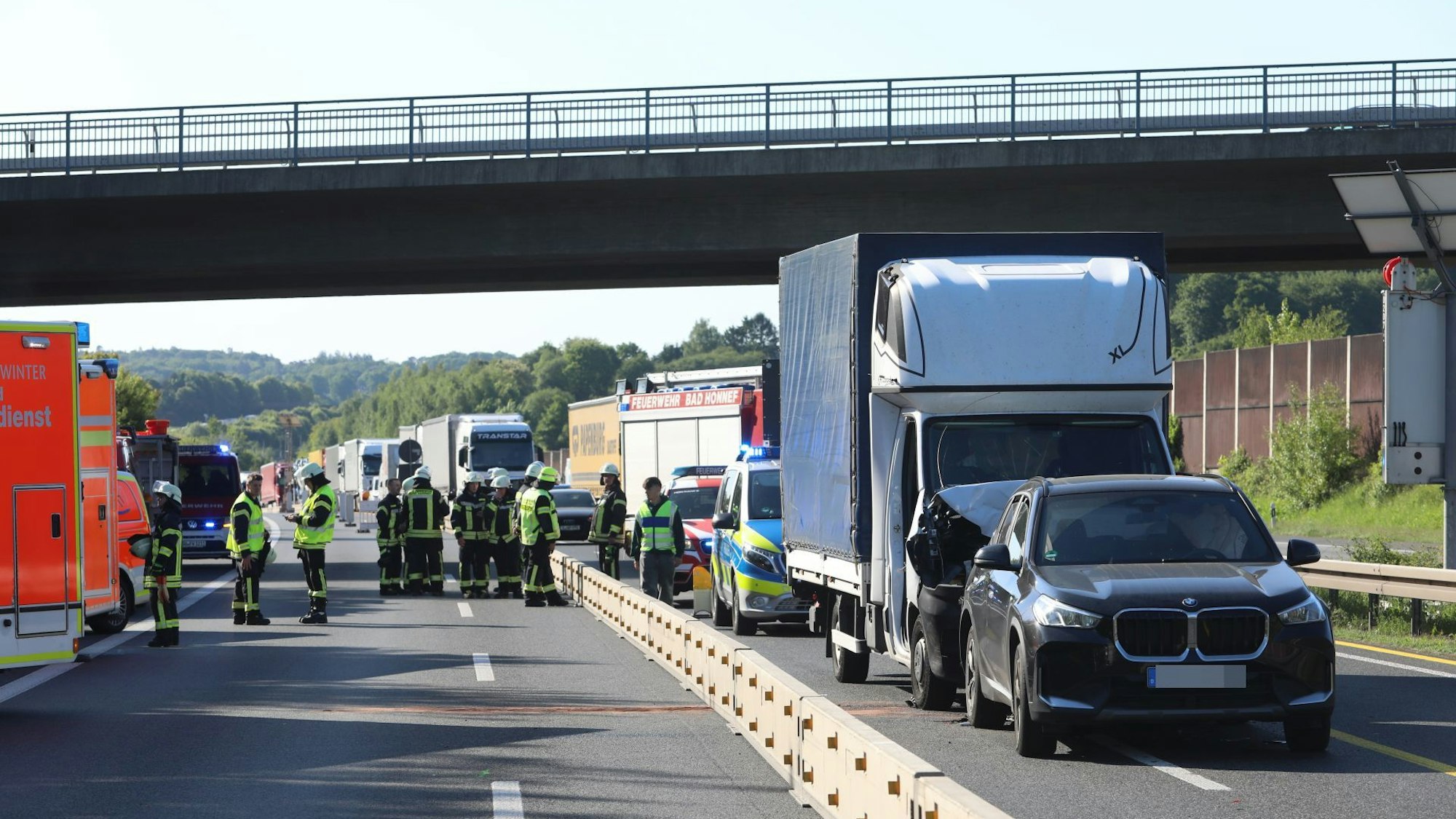 Ein Transporter und ein Pkw sind zusammengestoßen, dahinter staut sich der Verkehr, auf den gesperrten Spuren links daneben stehen Feuerwehrleute und Einsatzfahrzeuge.