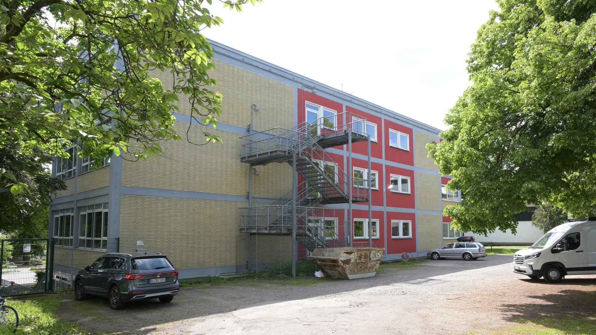 zwischen Bäumen und parkenden Autos ist die Gemeinschaftsgrundschule Bergisch Gladbach-Gronau zu sehen.