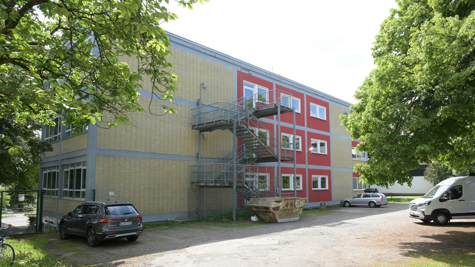 zwischen Bäumen und parkenden Autos ist die Gemeinschaftsgrundschule Bergisch Gladbach-Gronau zu sehen.