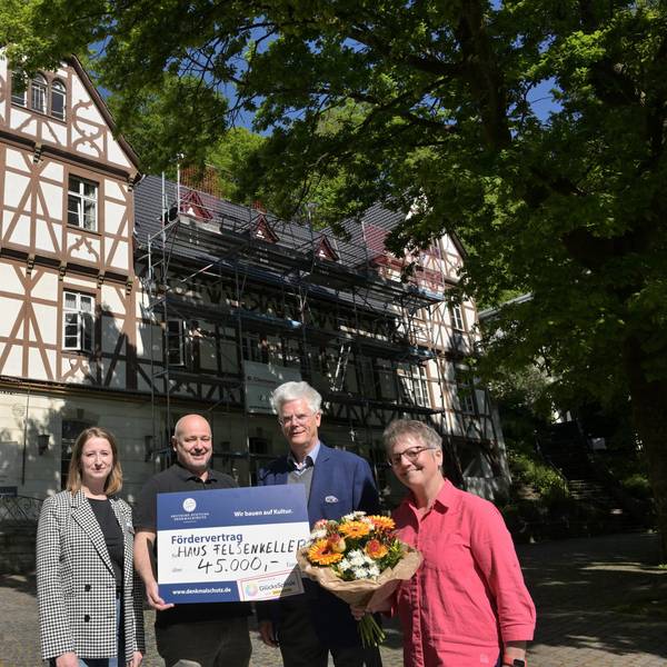 Vier Menschen stehen mit einem großen Scheck vor einem historischen Fachwerkgebäude.