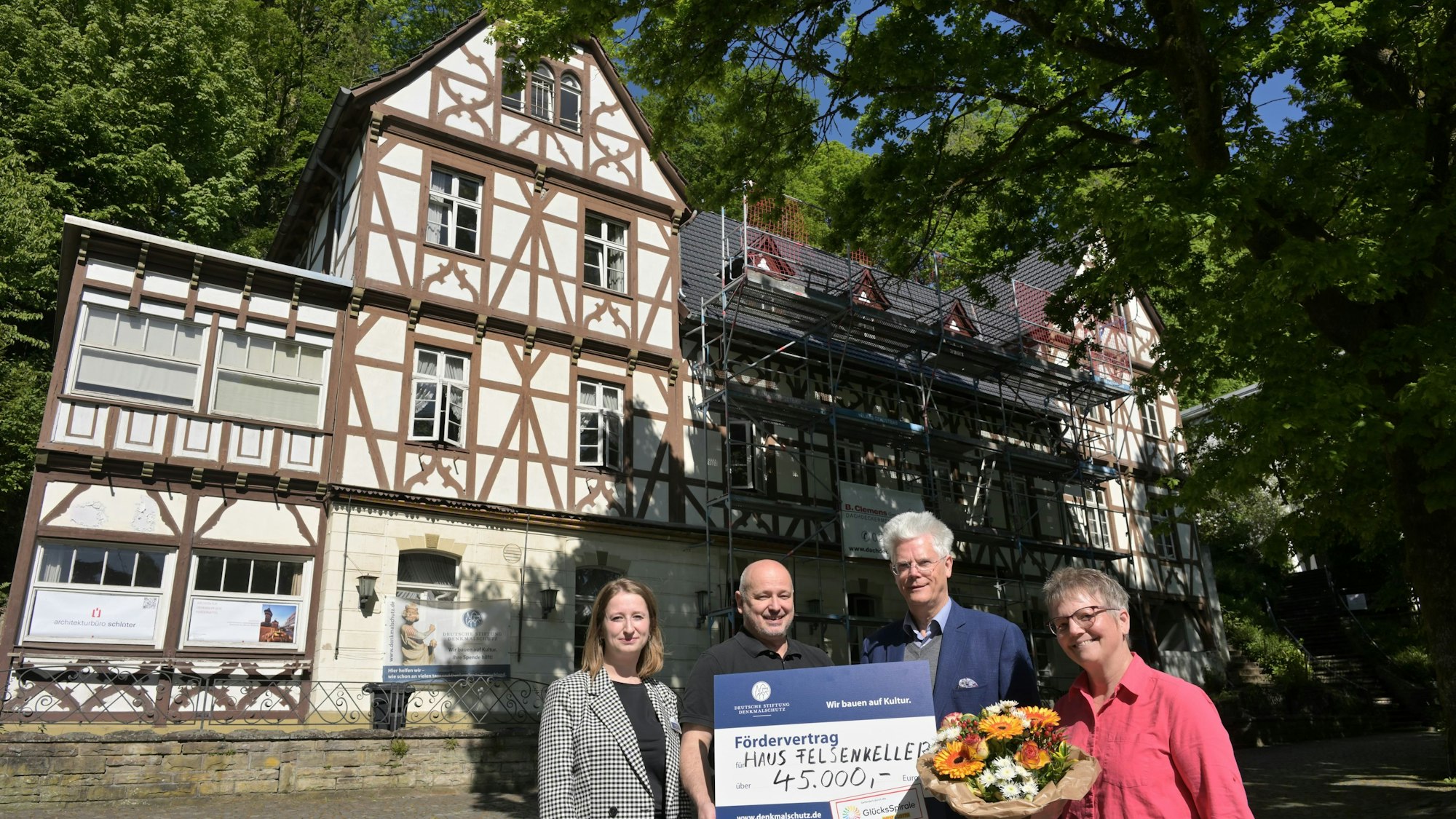 Vier Menschen stehen mit einem großen Scheck vor einem historischen Fachwerkgebäude.