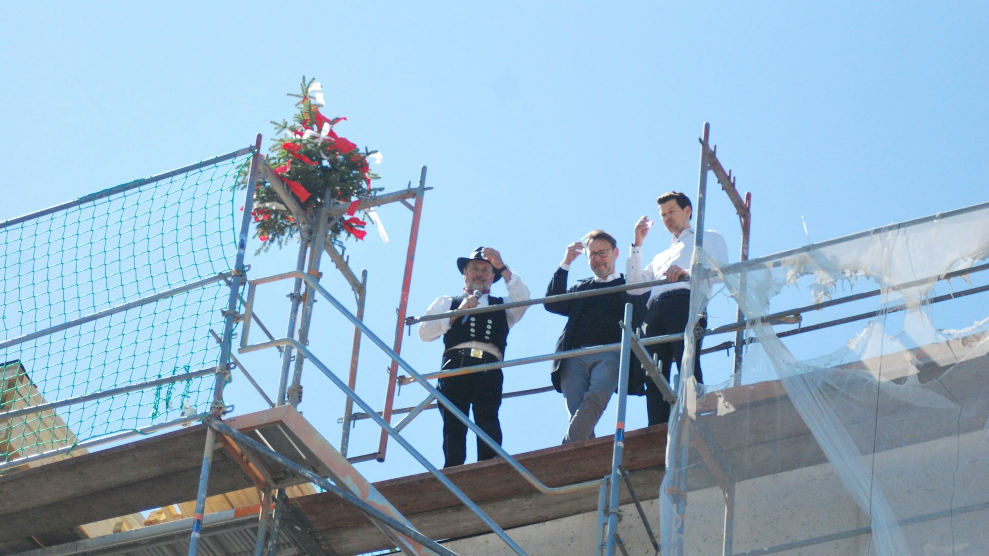 Das Bild zeigt den Zimmermann und zwei weitere Männer auf dem Dach des Neubaus. Sie prosten den Zuschauern zu.