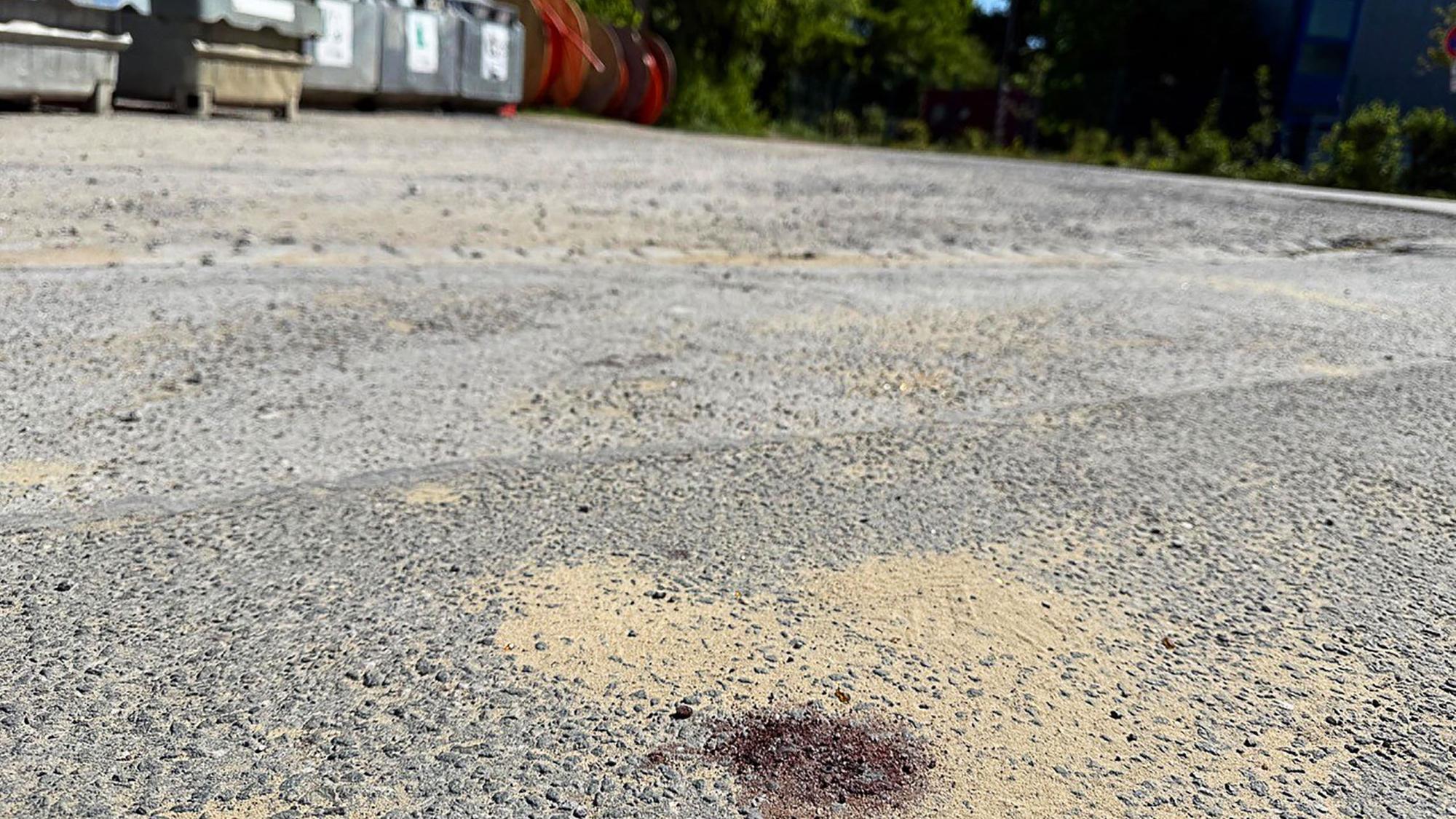Ein Blutfleck ist auf dem Asphalt am Tatort in Menden im Sauerland zu sehen. Nach dem gewaltsamen Tod eines 14-Jährigen ermittelt die Polizei.