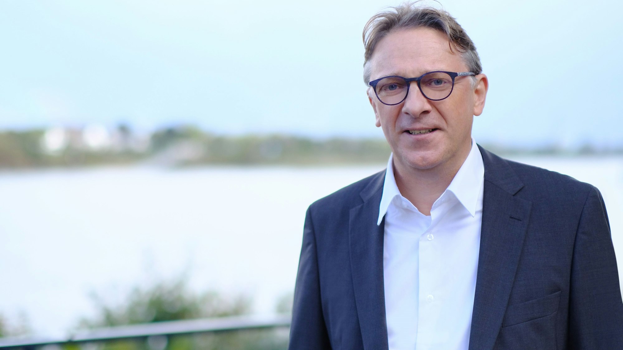 Auf dem Foto ist ein Mann mit grauem Harr zu sehen. Im Hintergrund ist unscharf ein Fluss zu erkennen.