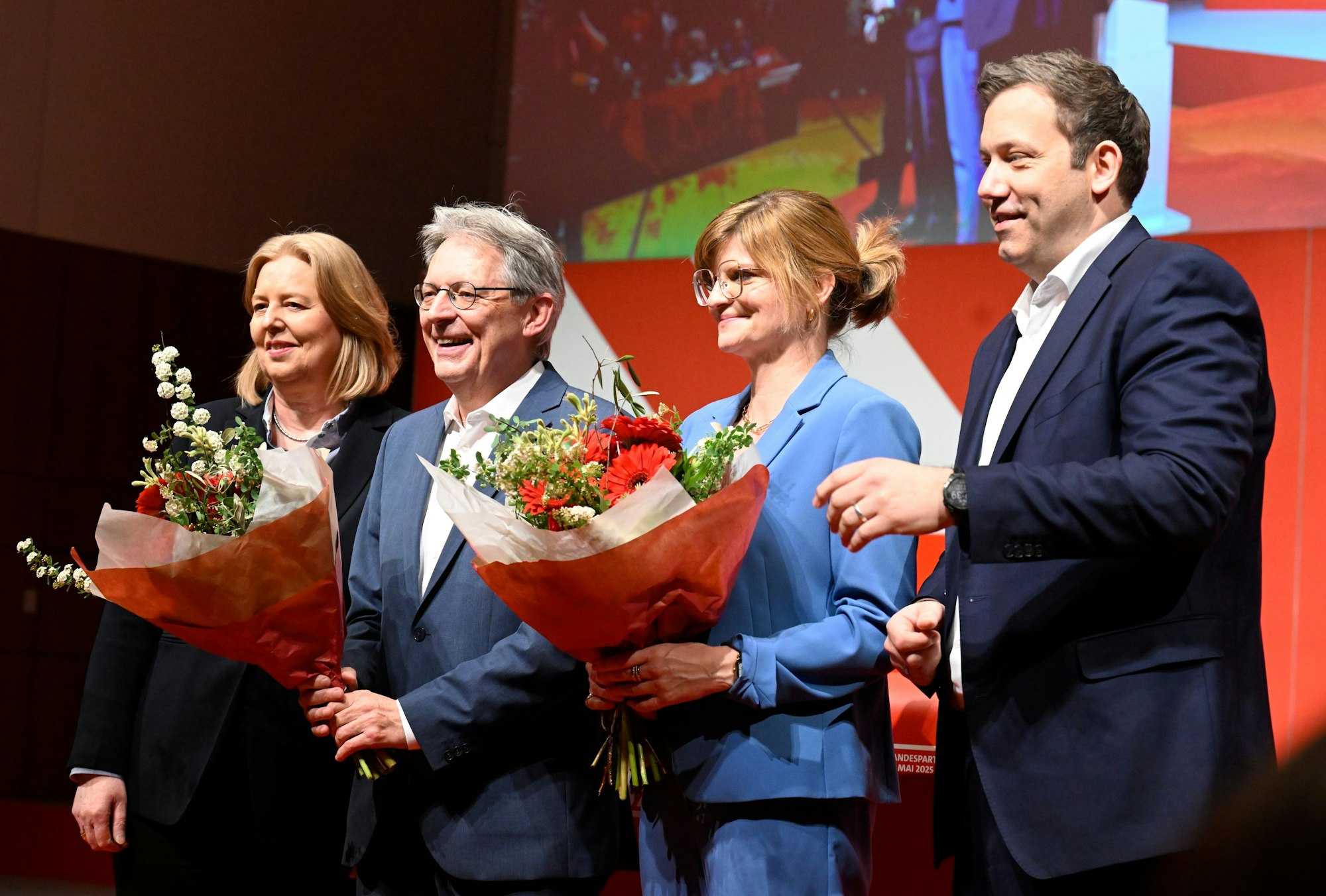 Achim Post (2.v.l.) und Sarah Philipp (2. v.r.) sind die Landesvorsitzenden der NRW-SPD. Sie stehen mit anderen Politikern auf einer Bühne und halten Blumensträuße in der Hand nach ihrer Wiederwahl.