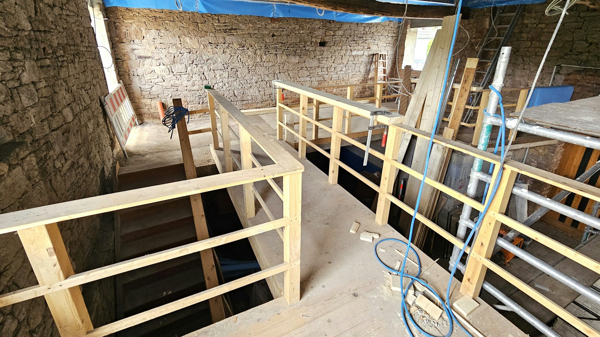 Ein mit Holzgeländern gesicherter Gang führt im Obergeschoss der Scheune zu einer Empore mit Holzboden. Die Außenwände sind unverputzt.