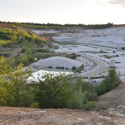 Das Bild zeigt die Aussicht über die Quarzgruben: ein steiler, weißer Abhang und daneben Bewaldung.