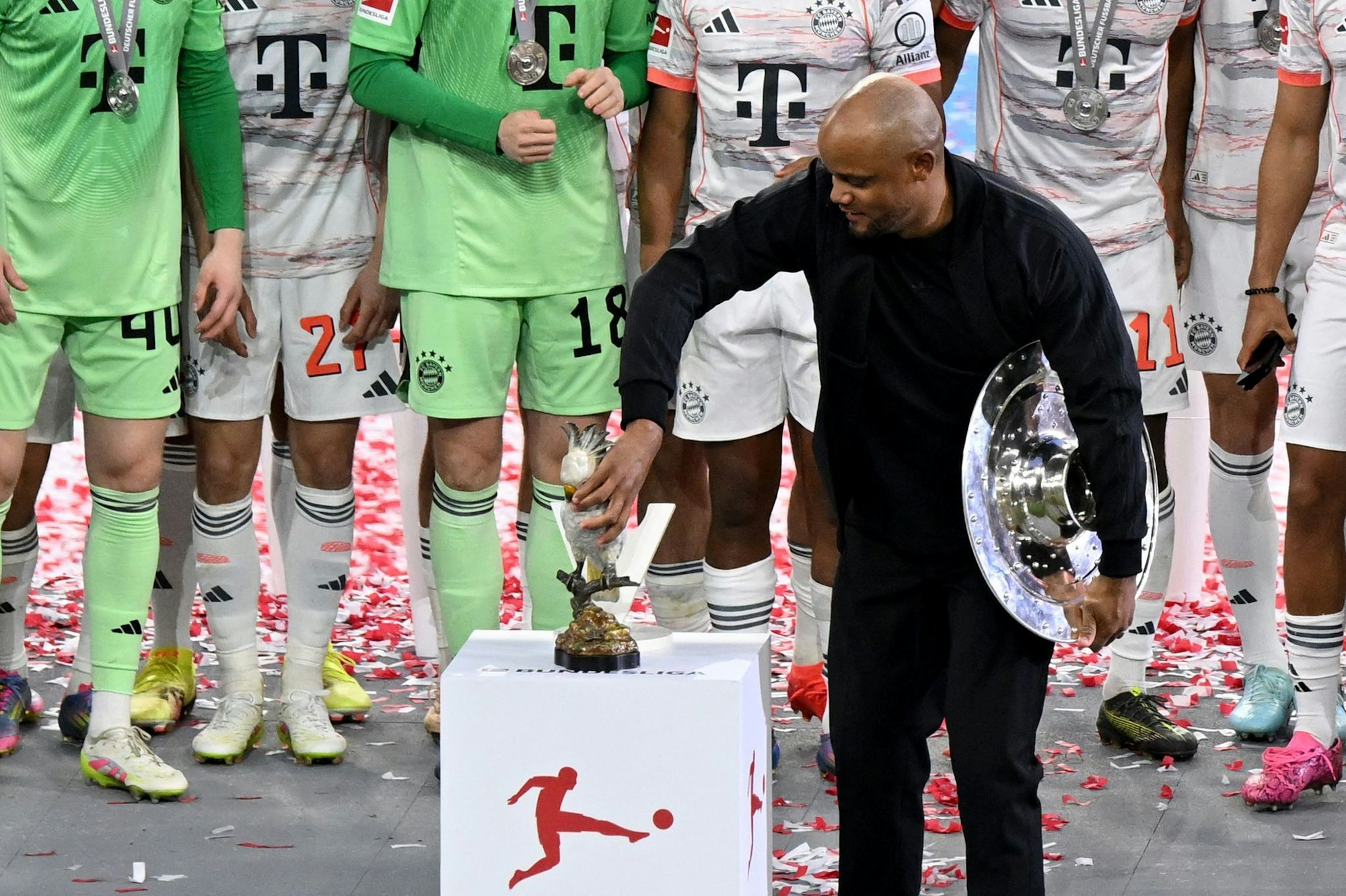 Bayern-Trainer Vincent Kompany stellt bei der Meisterparty eine Kakadu-Figur auf den Sockel.