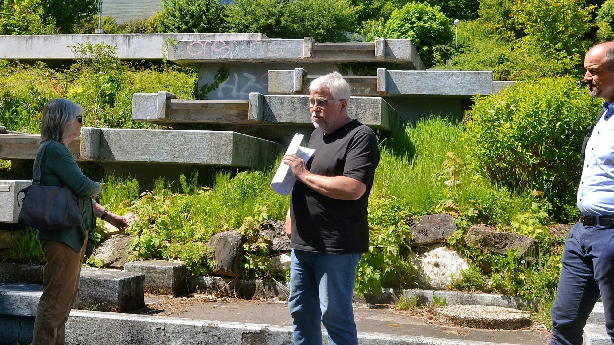 Zwei Männer und eine Frau vor einer Wasserterrasse aus Beton im Kurgarten von Bad Münstereifel.
