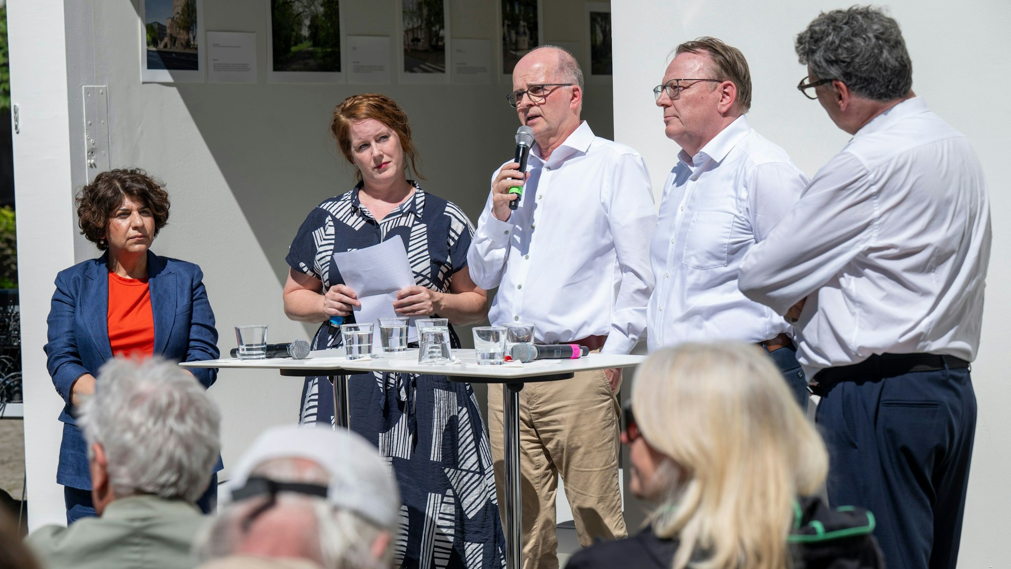 Auf dem Bild sind drei Kölner OB-Kandidaten der Grünen, SPD und CDU und die beiden Moderatoren des KSTA an einem Stehtisch zu sehen.