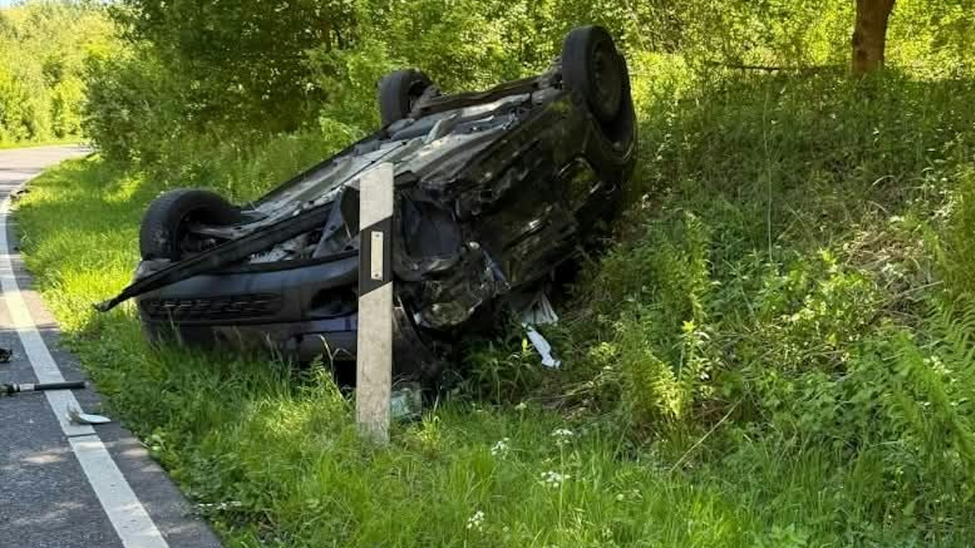 Zu sehen ist ein auf dem Dach liegendes Auto im Straßengraben.