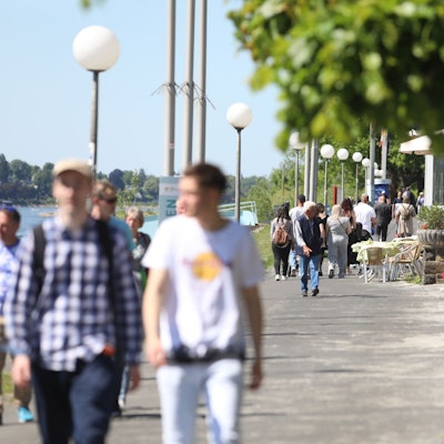 Menschen flanieren über die Rheinpromenade, andere sitzen in der Außengastronomie.