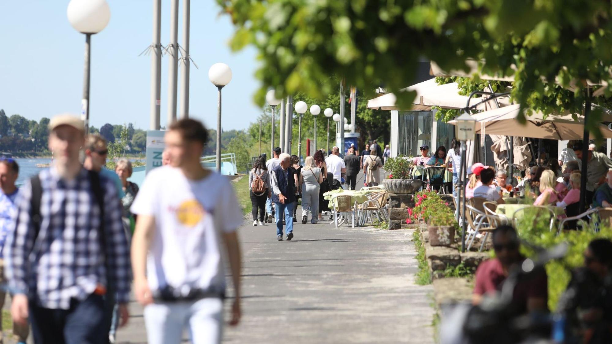 Menschen flanieren über die Rheinpromenade, andere sitzen in der Außengastronomie.