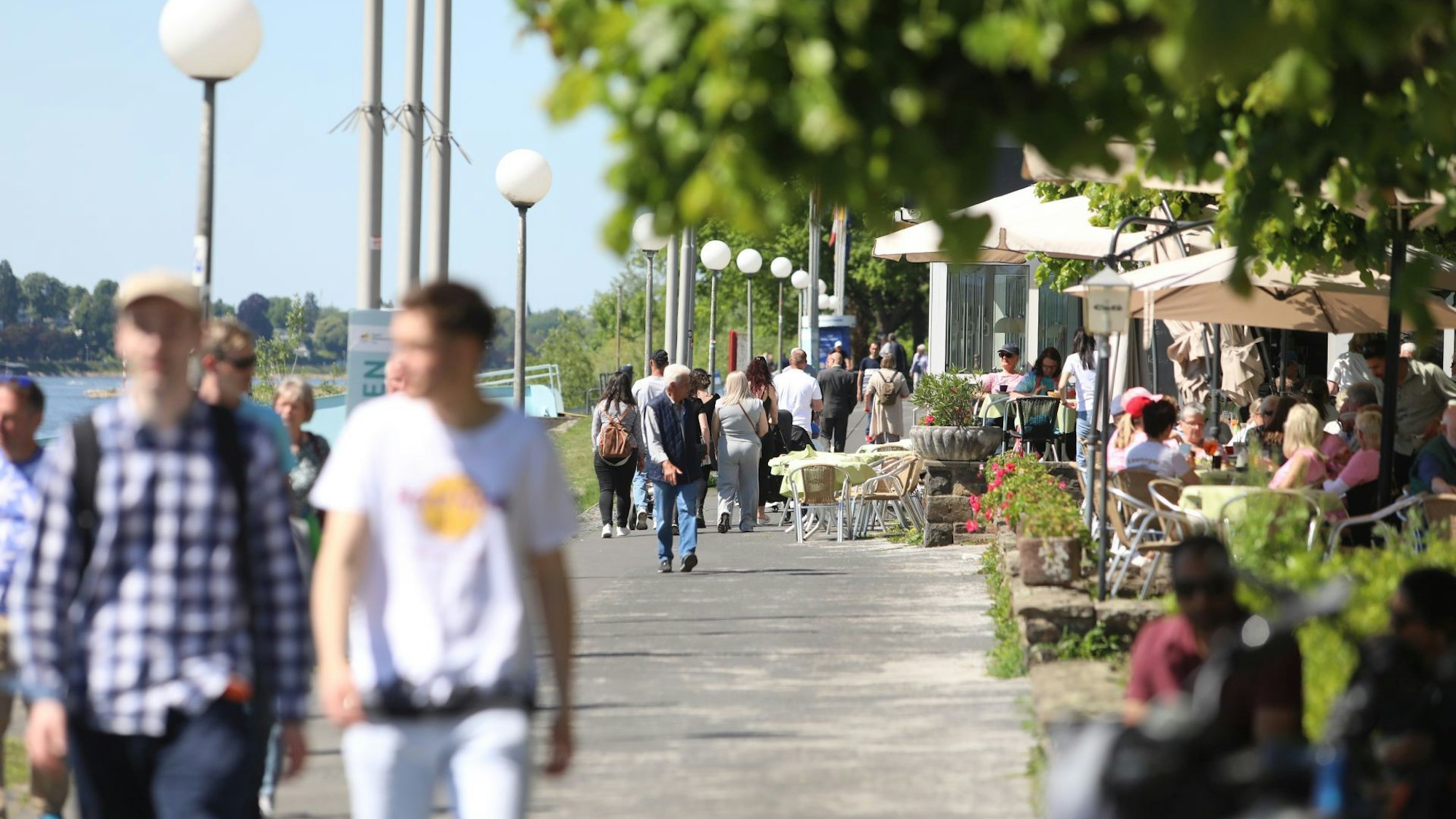 Menschen flanieren über die Rheinpromenade, andere sitzen in der Außengastronomie.
