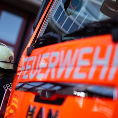 Eine Einsatzkraft der Feuerwehr steht neben einem Einsatzfahrzeug der Feuerwehr.