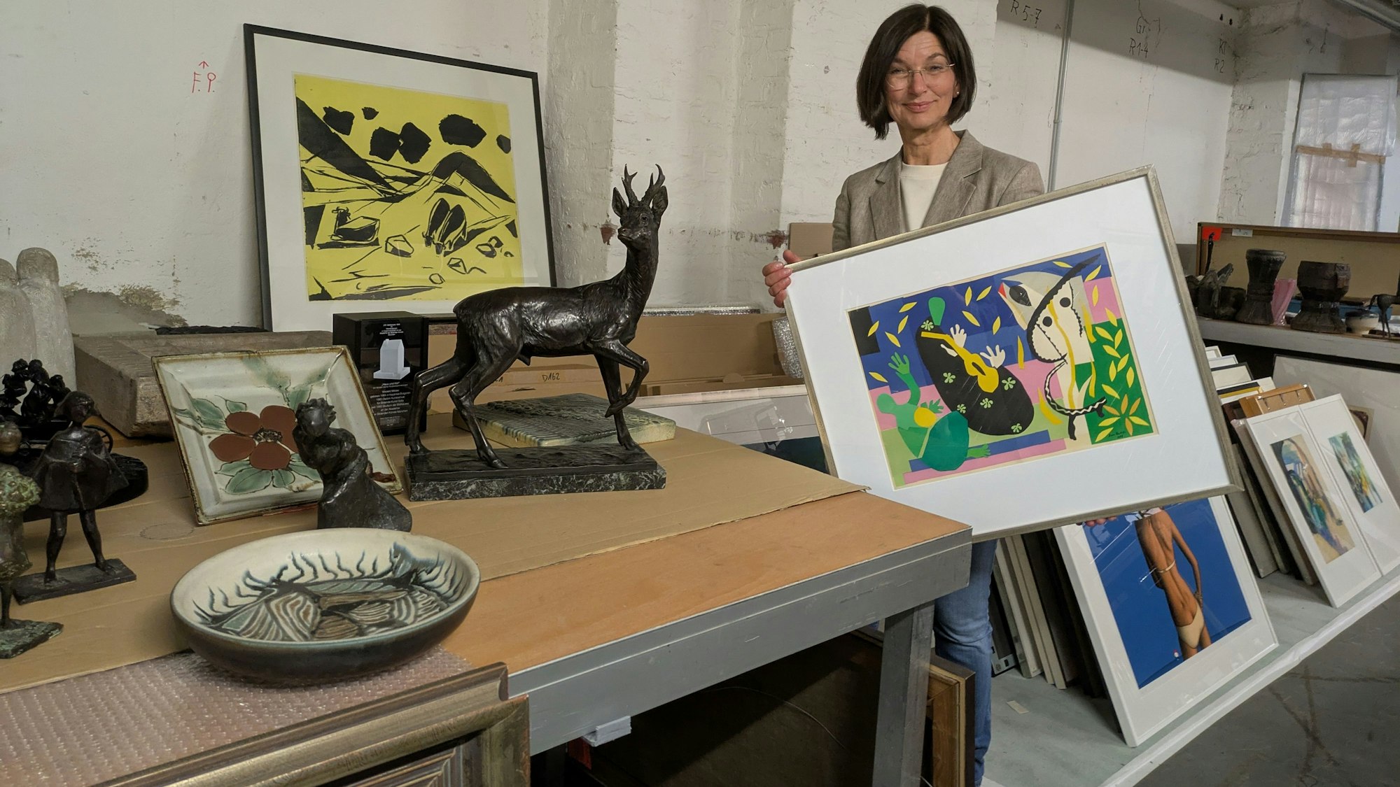 Eine Frau zeigt umgeben von Kunstwerken eine Grafik.