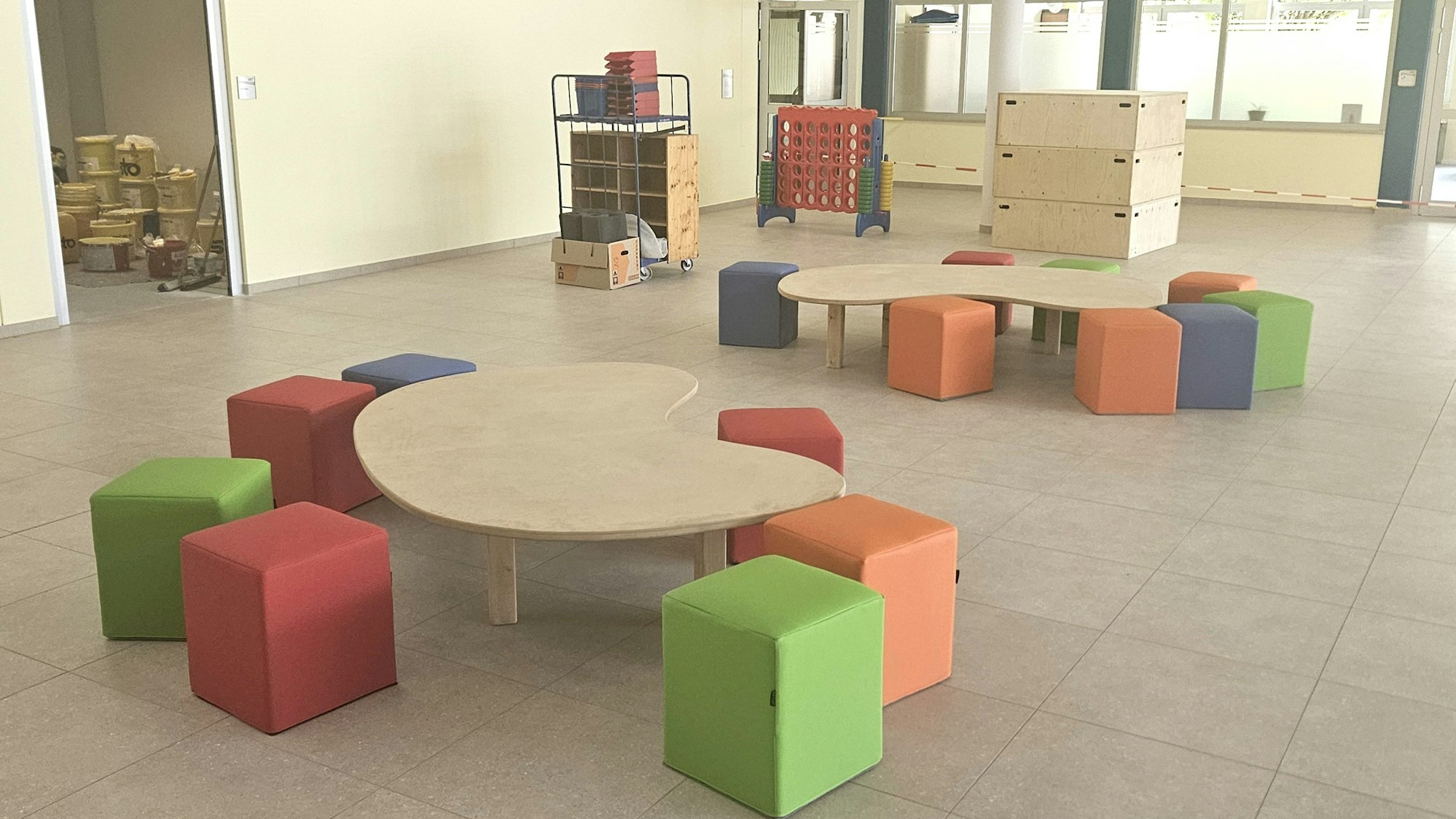 Sitzhocker stehen im Foyer um Holztische herum