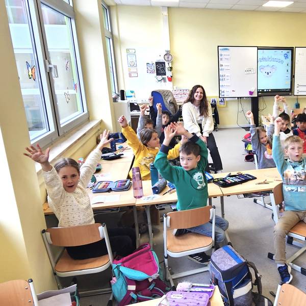 Die Kinder der Klasse 2a der Kaller Grundschule sitzen in ihrer Klasse und reißen die Arme hoch.