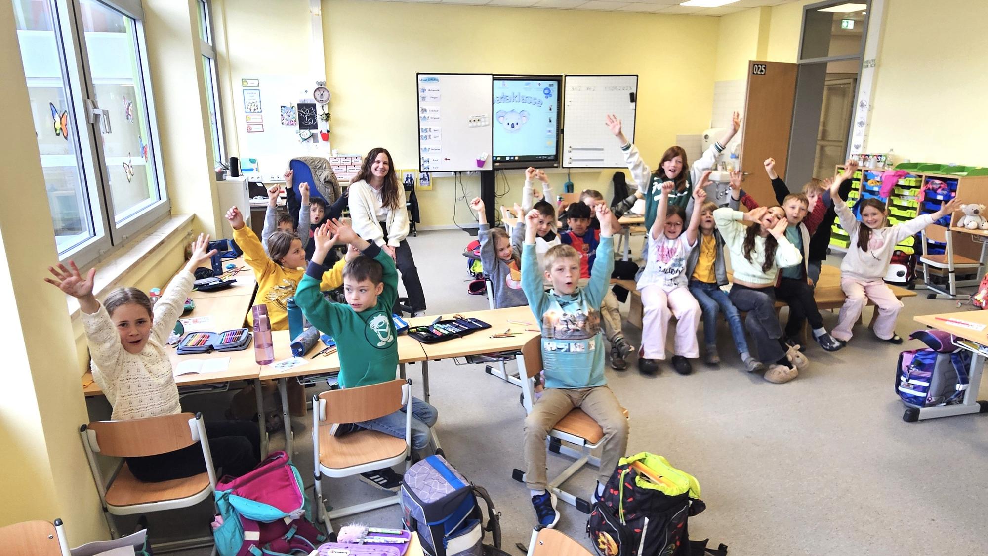 Die Kinder der Klasse 2a der Kaller Grundschule sitzen in ihrer Klasse und reißen die Arme hoch.