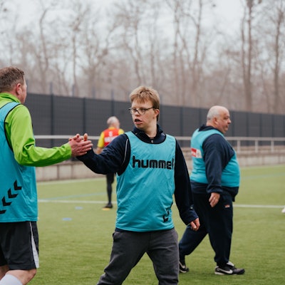 Auf dem Bild sind Sportler auf einem Rasenfeld zu sehen, die beim Inklusionssport des 1. FC Köln mitmachen.