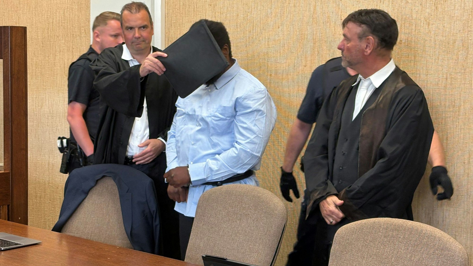 Der Angeklagte, hier mit seinen Verteidigern, wurde zunächst gefesselt in den Gerichtssaal geführt.