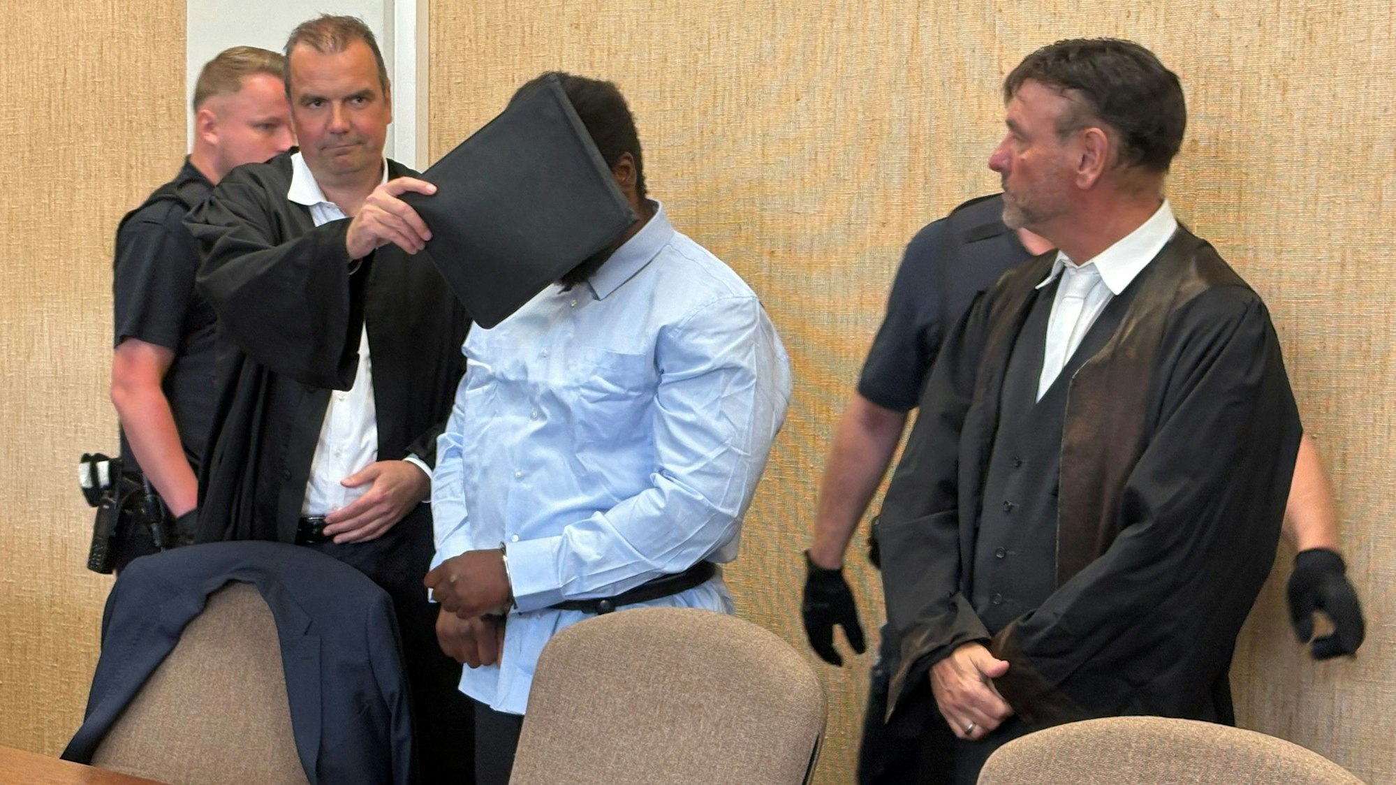 Der Angeklagte, hier mit seinen Verteidigern, soll einer Polizistin ein Stück vom Ohr abgebissen haben.