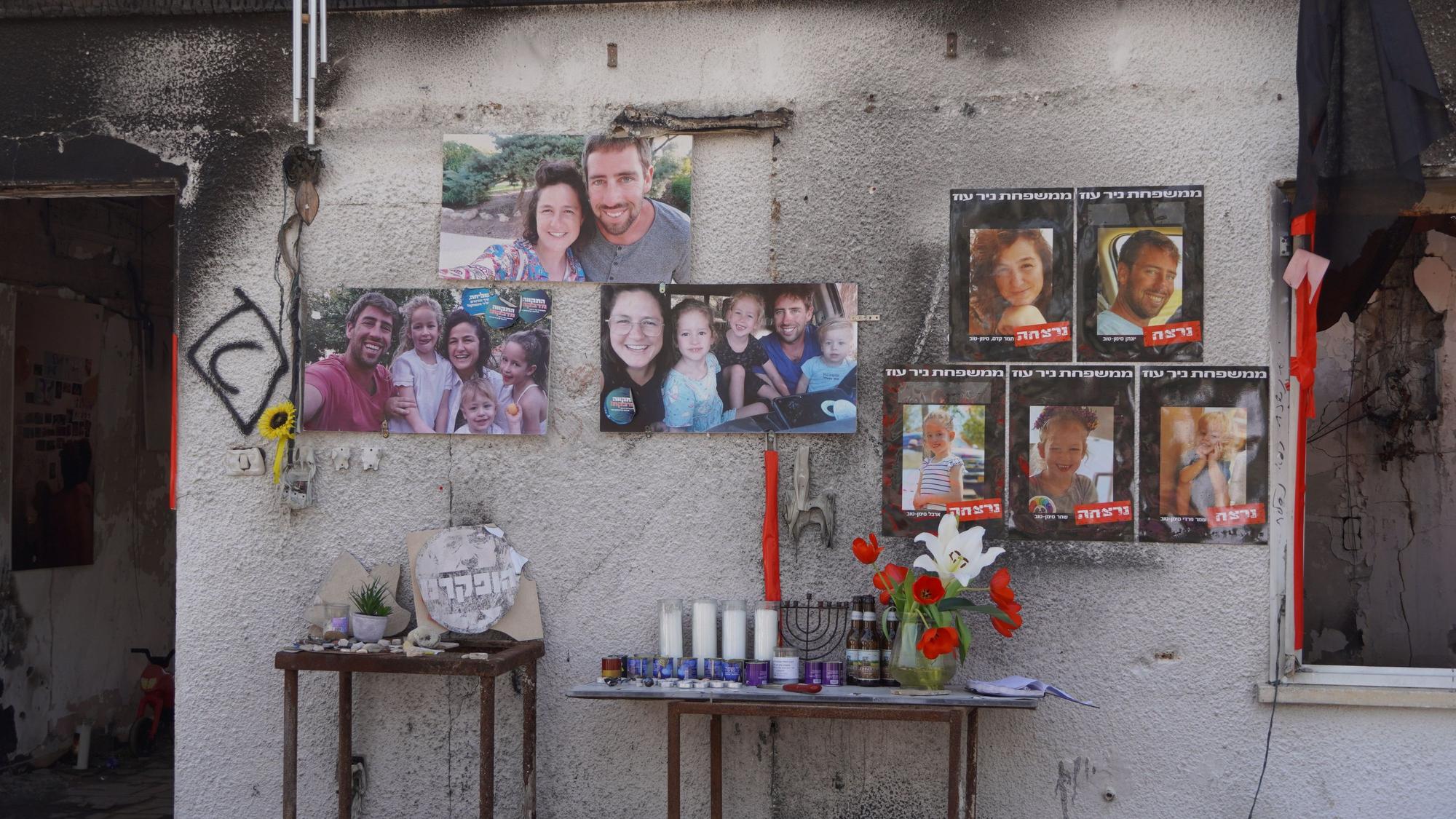 Bilder von Familien und Porträts einzelner Kinder und junger Männer hängen an einer rußgeschwärzten Häuserwand, davor sind Tische mit Kerzen, Blumen und jüdischen Kerzenleuchtern.