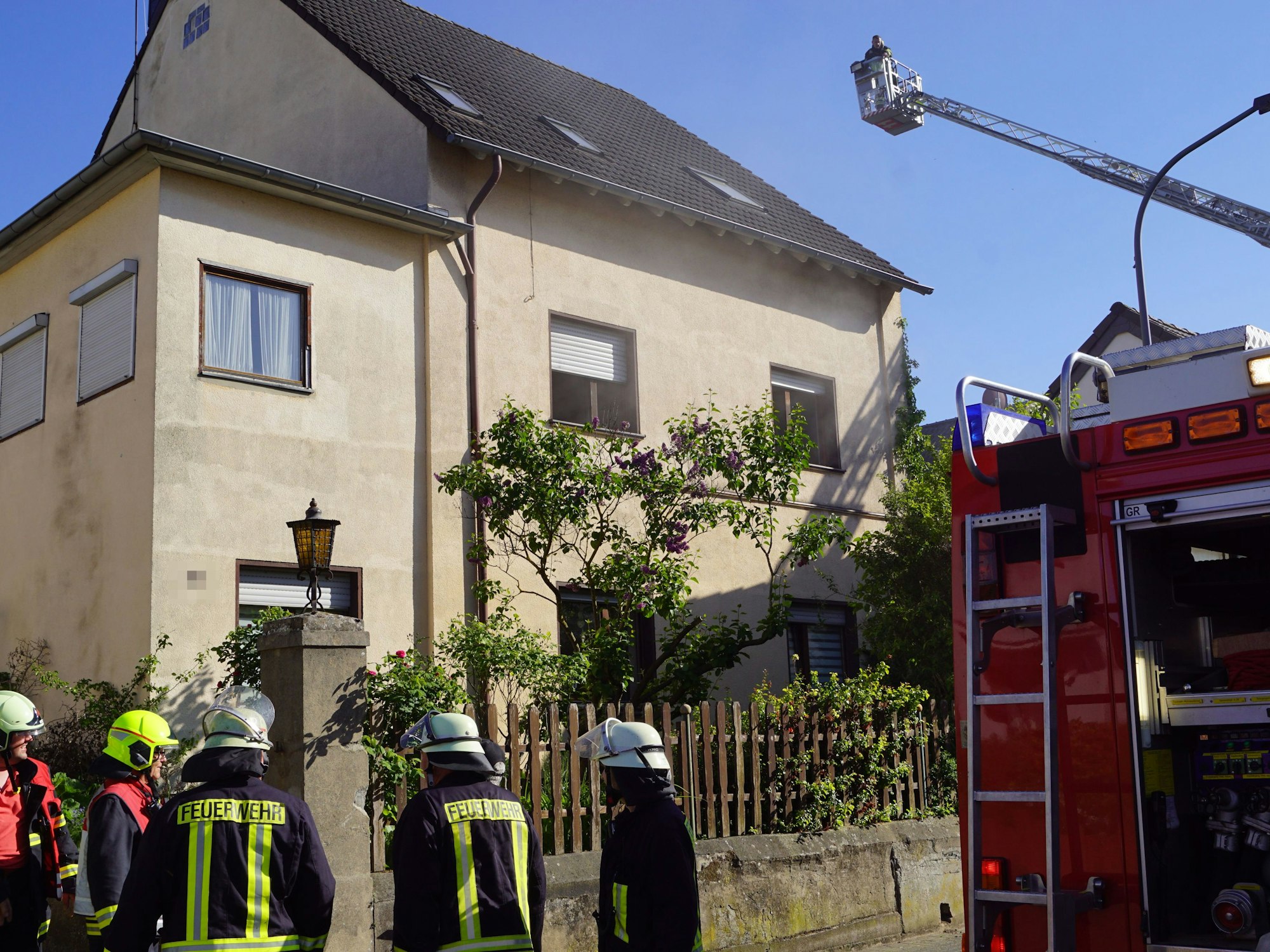 Feuerwehrleute besprechen die Lage vor dem Haus. Im Korb einer ausgefahrenen Drehleiter beobachtet ein Feuerwehrmann das Haus.