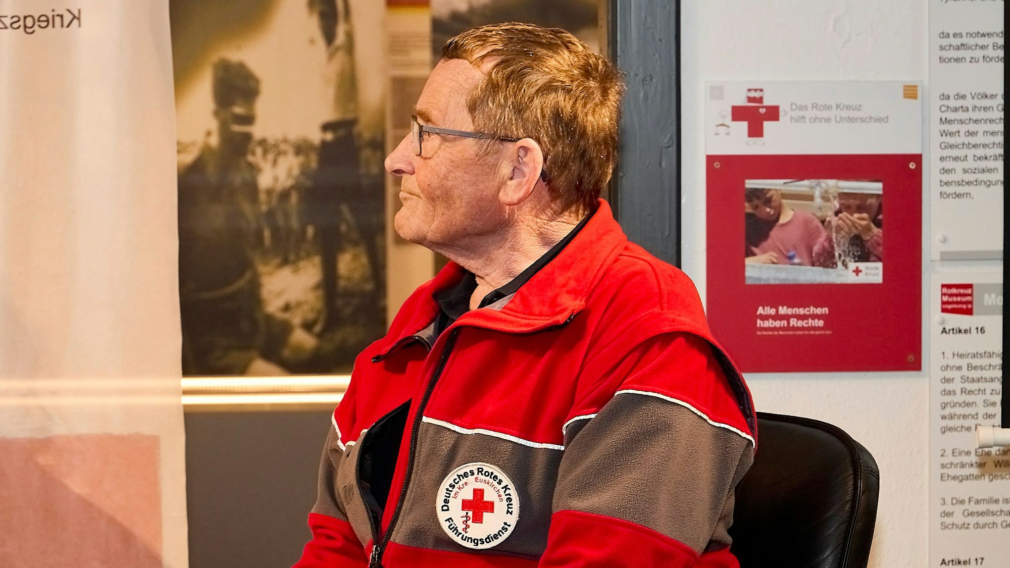 Ein Mann in Rotkreuzkleidung sitzt auf einem Stuhl.