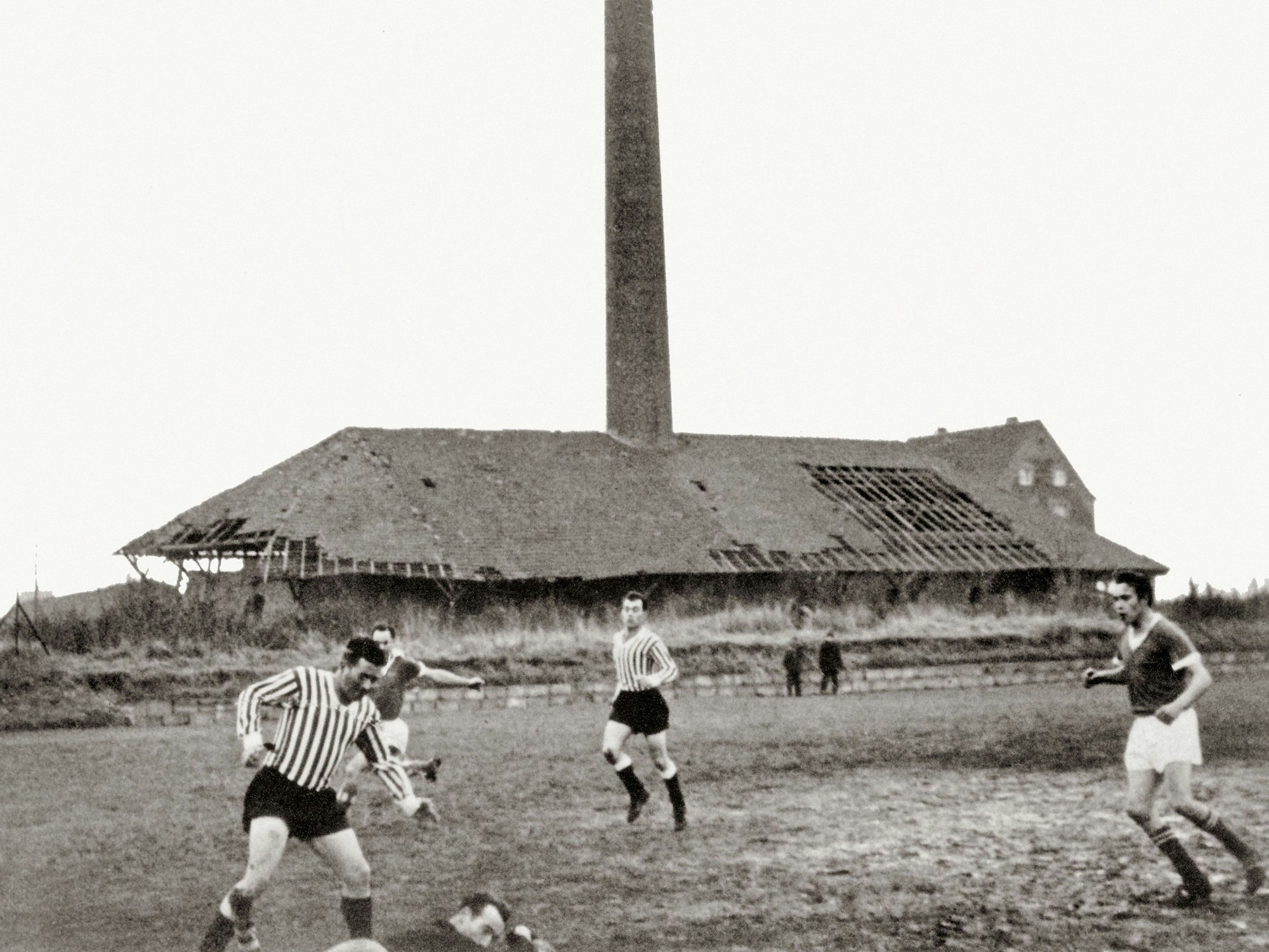 Vor dem verfallenden Gebäude einer Ziegelei spielen Männer Fußball.