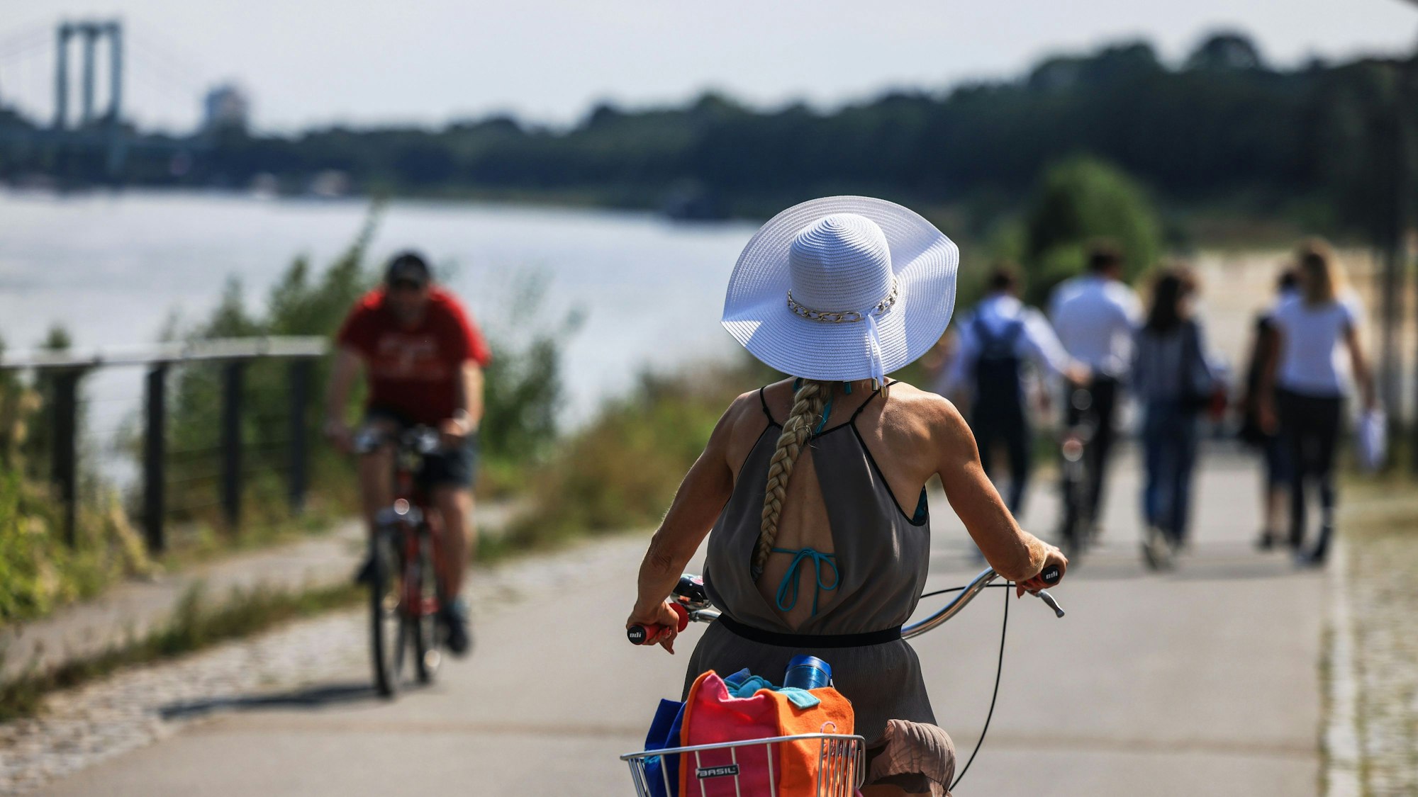 Eine Radfahrerin fährt mit Sonnenhut am Rheinufer entlang.