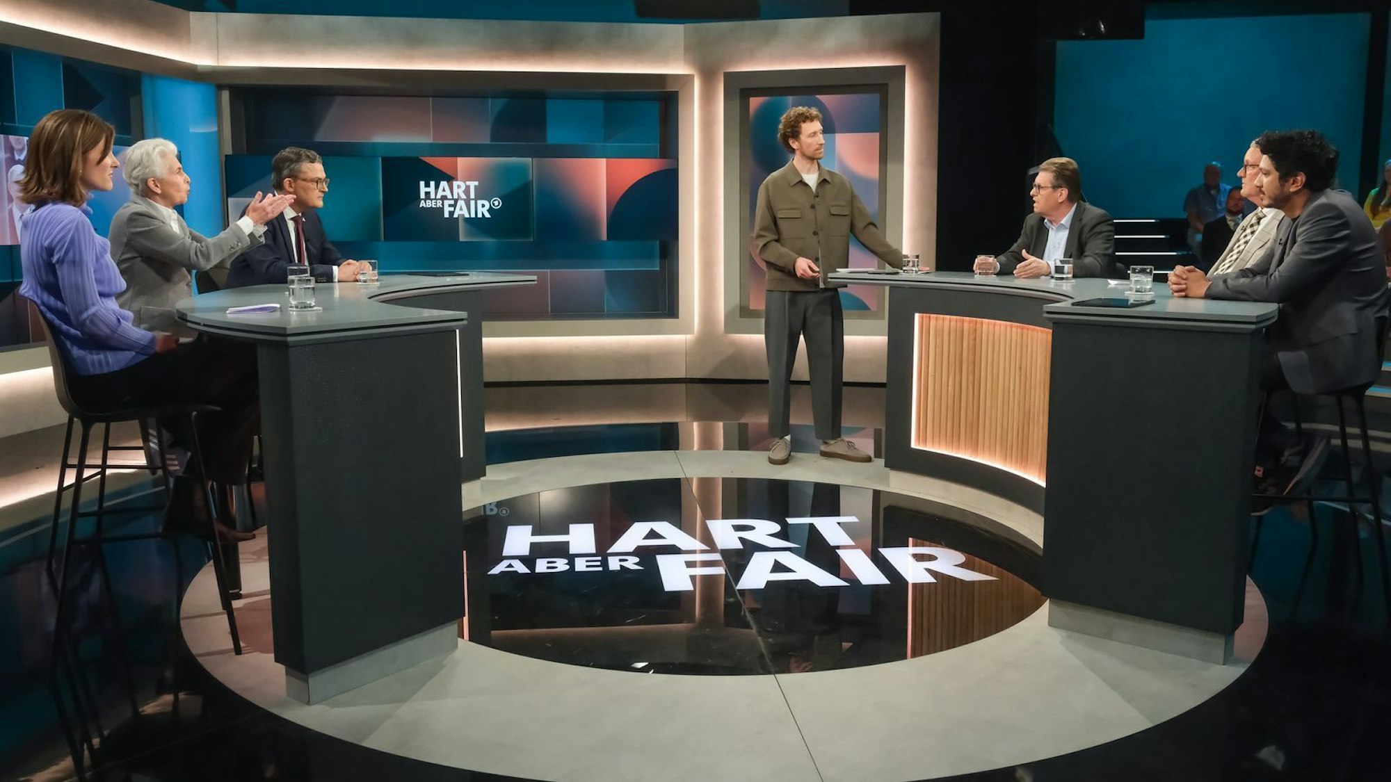 „Hart aber fair“ am Montagabend: Moderator Louis Klamroth (stehend) begrüßte seine Gäste (von links nach rechts) Sophie von der Tann, Marie-Agnes Strack-Zimmermann, Roderich Kiesewetter, Ralf Stegner, Michael Lüders und Jörg Wimalasena. (Bild: WDR/Oliver Ziebe)