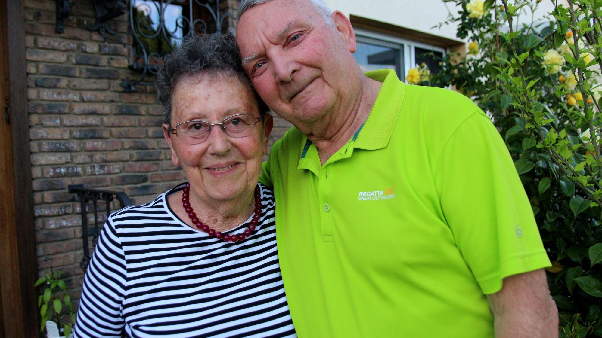 Ein Mann und eine Frau stehen vor einem Haus und lächeln.