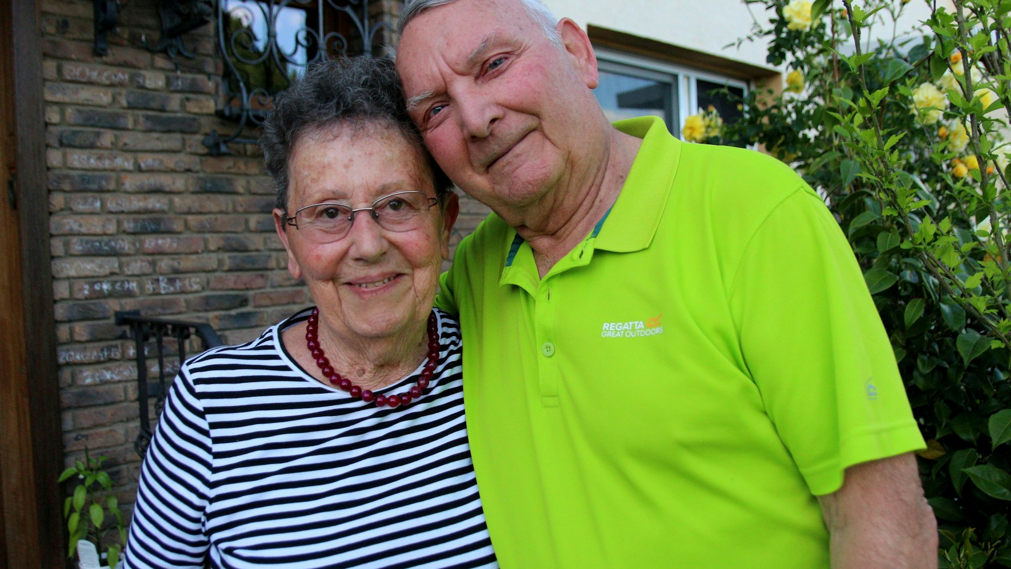 Ein Mann und eine Frau stehen vor einem Haus und lächeln.