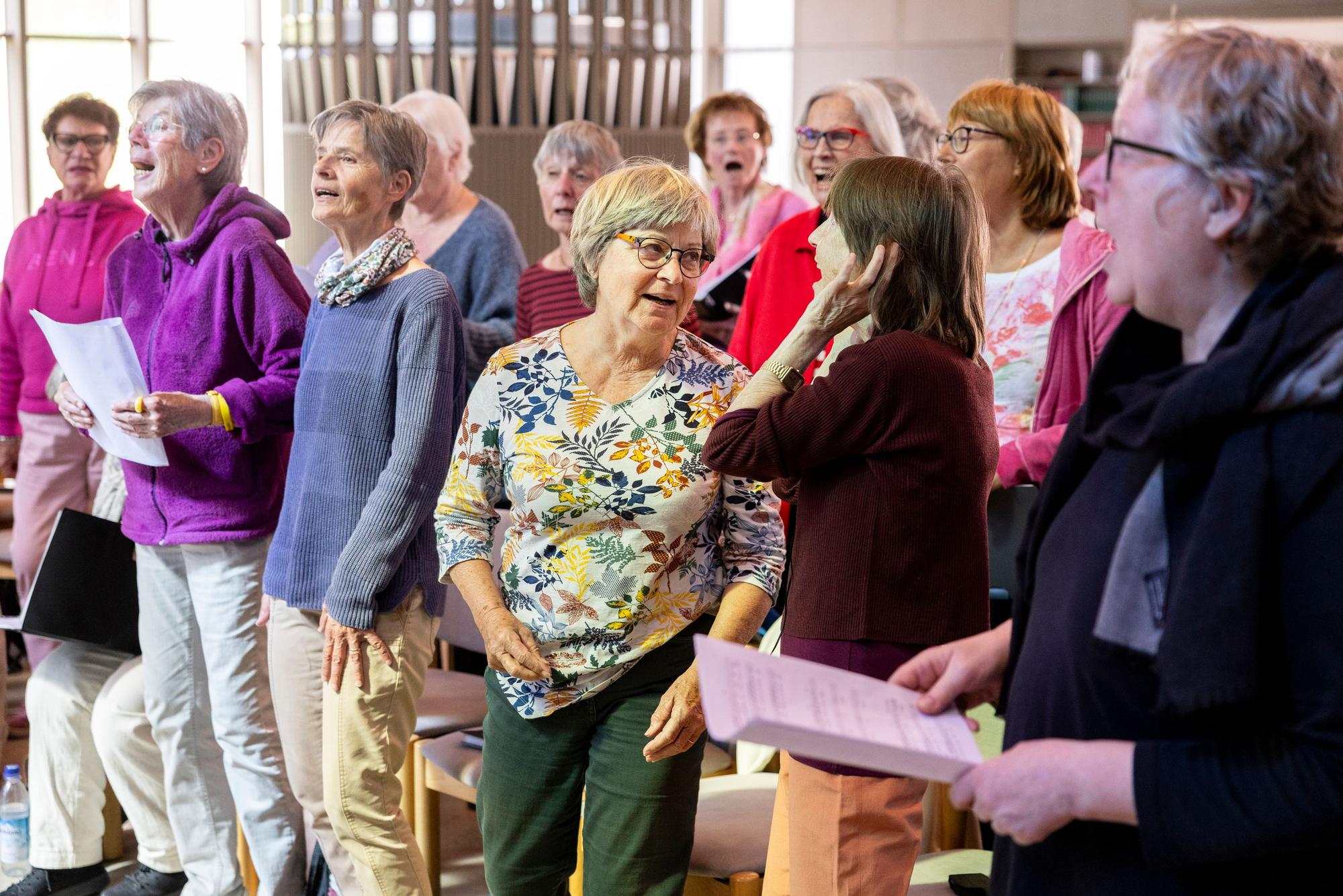 Die Chormitglieder sind singend zu sehen. Einige halten Noten in der Hand.