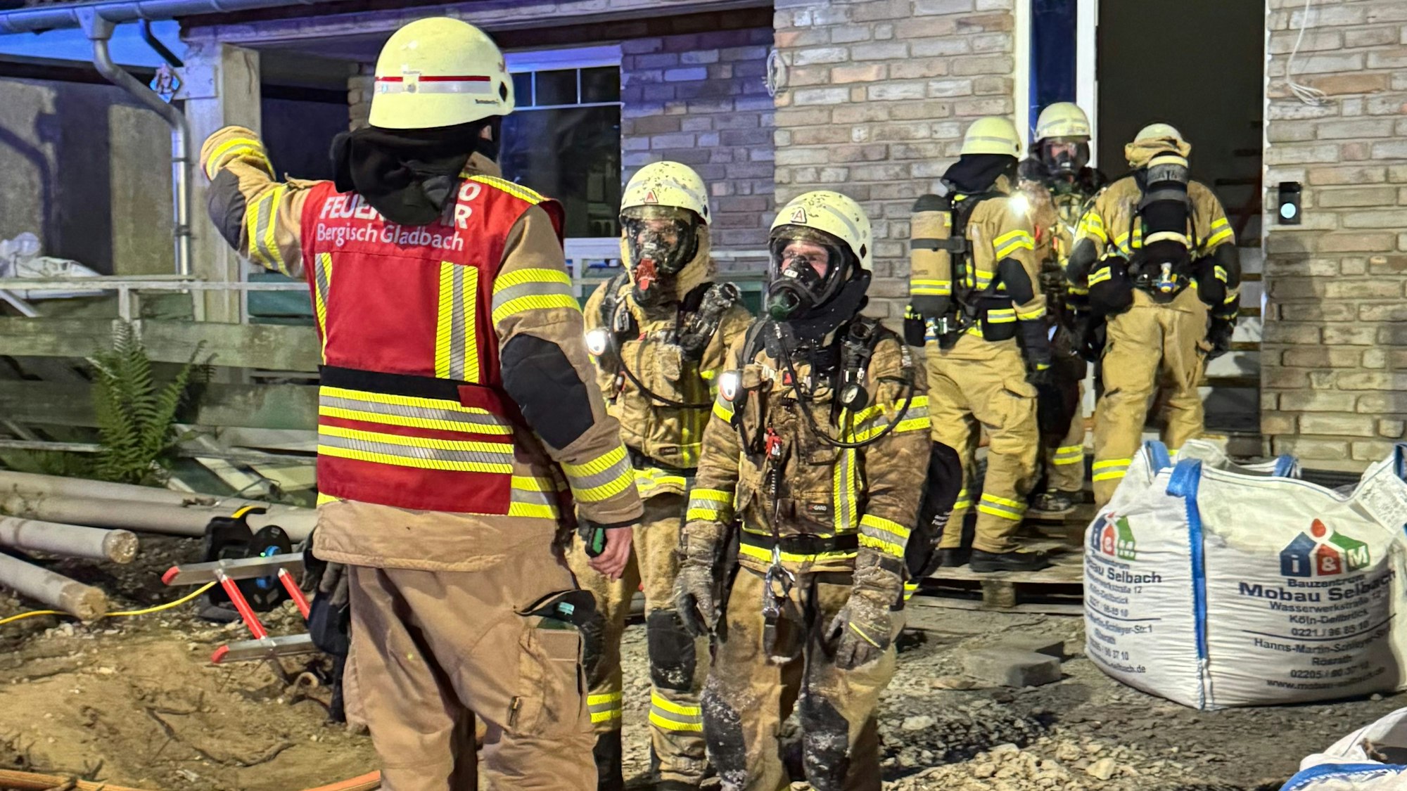 Feuerwehrleute stehen vor und am Eingang eines im Umbau befindlichen Gebäudes in Bergisch Gladbach-Kippekausen.