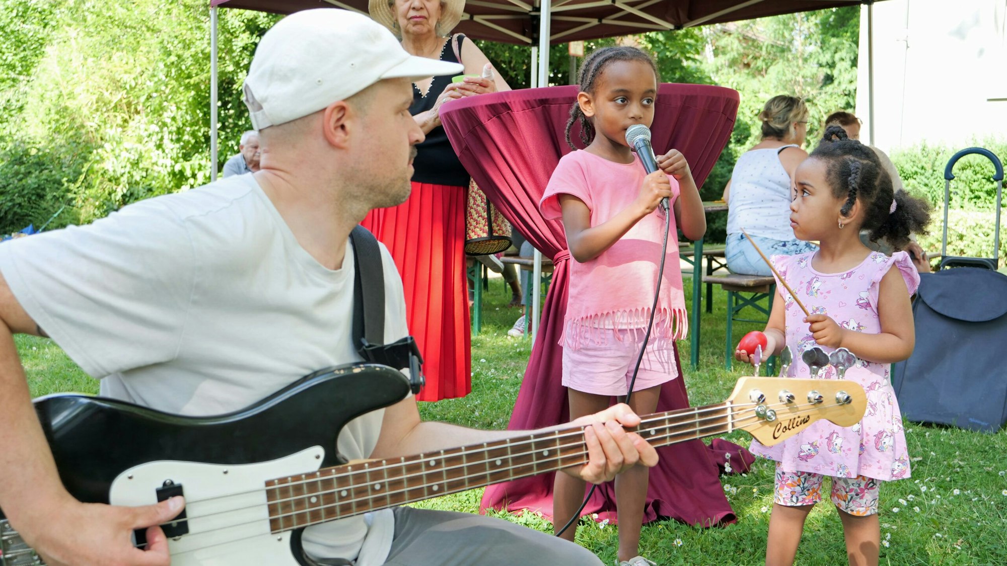 Ein Mann spielt Gitarre, zwei Mädchen singen und musizieren dazu.