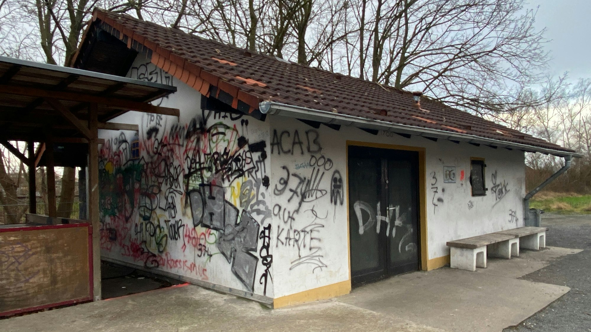 Man sieht ein kleines Haus, das mit vielen Schmierereien überzogen ist und an der linken Seite einen hölzernen Anbau hat.