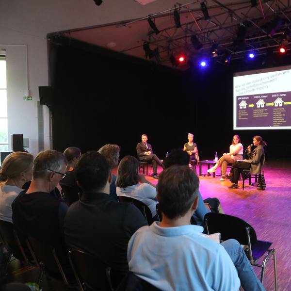Menschen sitzen in der Alten Feuerwache und folgen der Informationsveranstaltung „Wie funktioniert eine Erstaufnahmeeinrichtung?“.