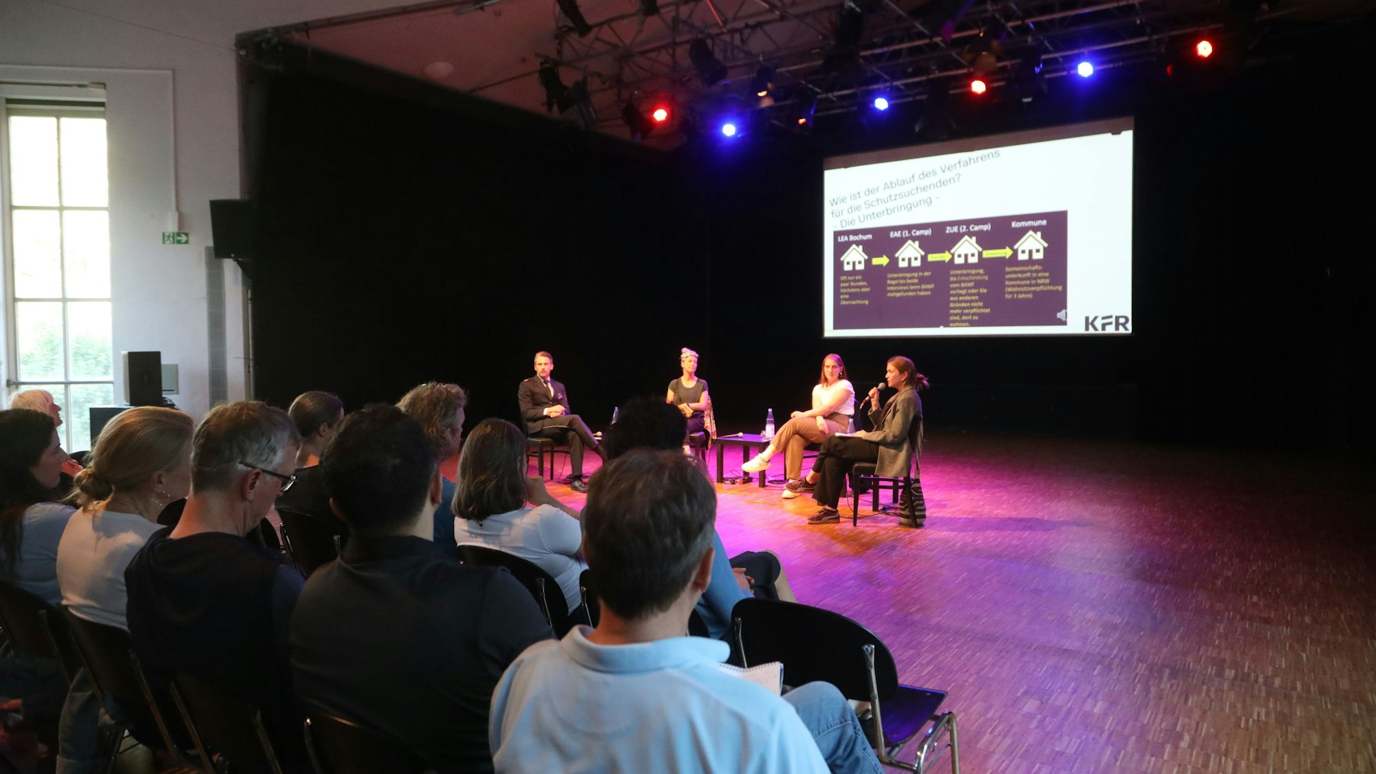 Menschen sitzen in der Alten Feuerwache und folgen der Informationsveranstaltung „Wie funktioniert eine Erstaufnahmeeinrichtung?“.