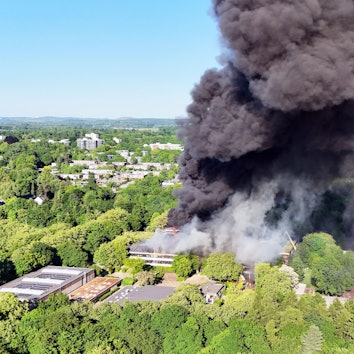 Eine schwarze Rauchwolke ist bei einem Großbrand über einem Gebäudekomplex mit mehreren Schulen im Kreis Mettmann zu sehen.